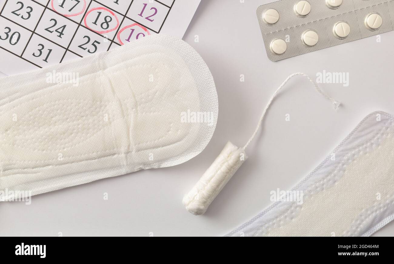 Background with various menstrual hygiene products, pills and personal hygiene with calendar with critical days for women on white background. Top vie Stock Photo