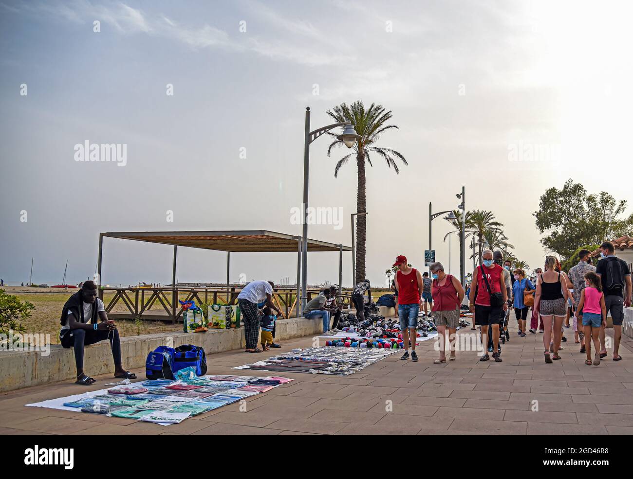 People walk in front of the stalls with blankets on the ground covered with  illegal products along Paseo Maritimo Street in Vendrell. Illegal street  vendors known as "manteros" or "Top Manta", mostly