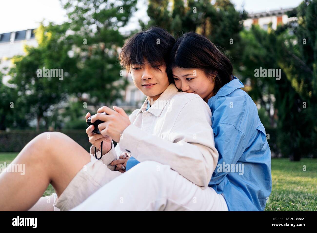 https://c8.alamy.com/comp/2GD486Y/cute-asian-couple-sitting-in-the-park-together-and-using-a-camera-2GD486Y.jpg