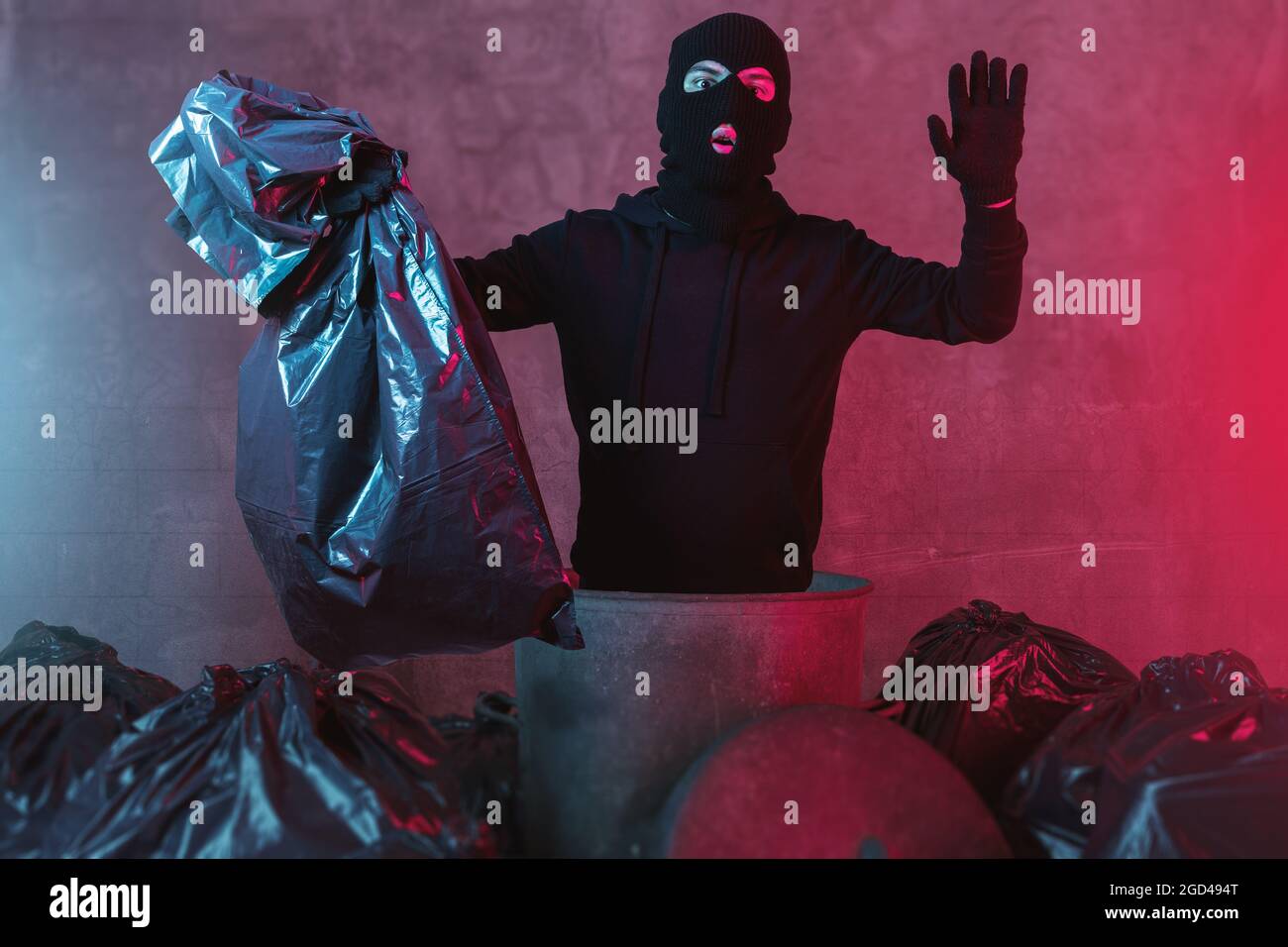 surprised thief comes out from garbage can and hold the hands up and get illuminated from the police lights Stock Photo