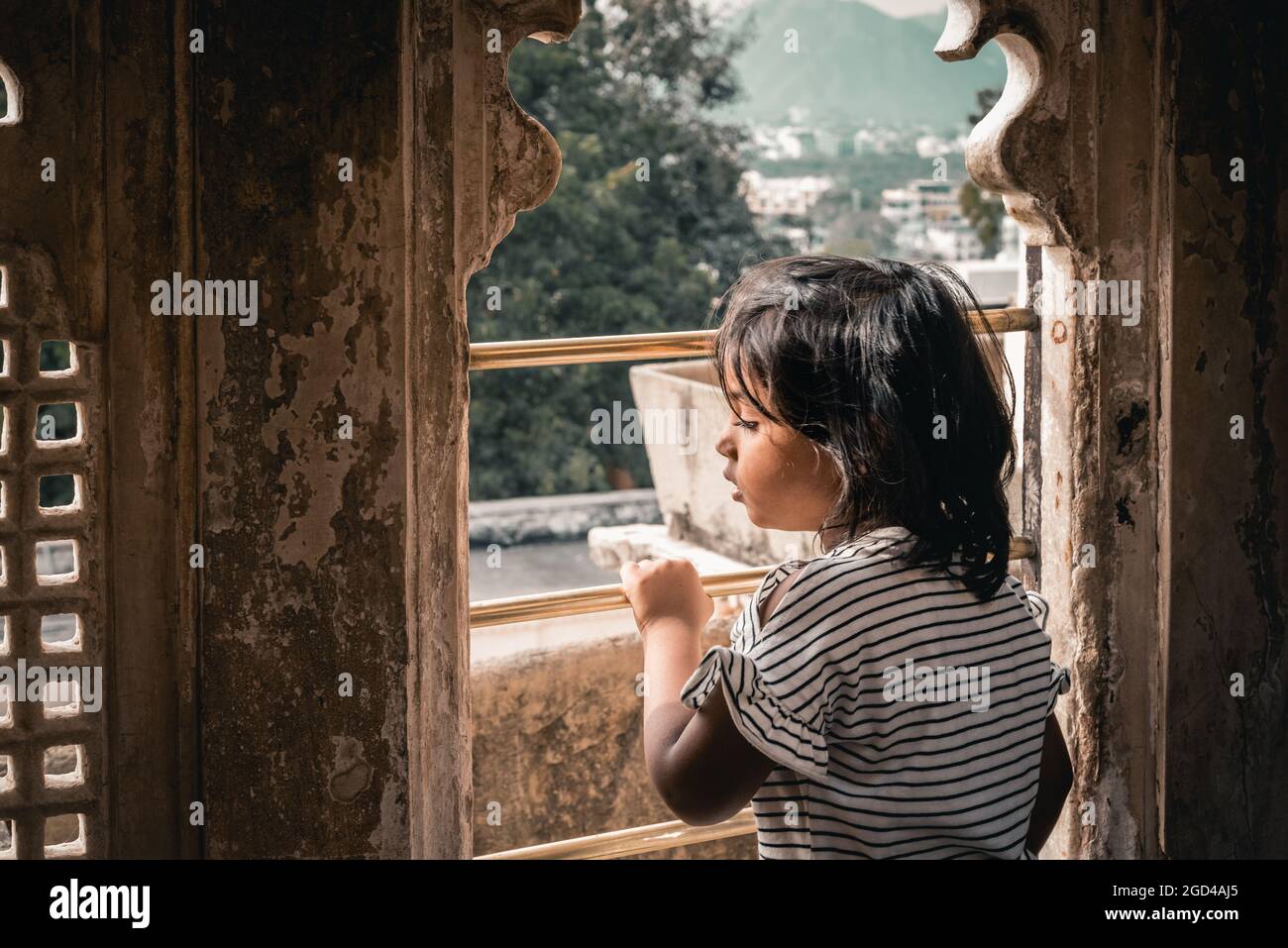 Colored portrait of a young girl child curiously looking out from a window of vintage architectural tourist building Stock Photo
