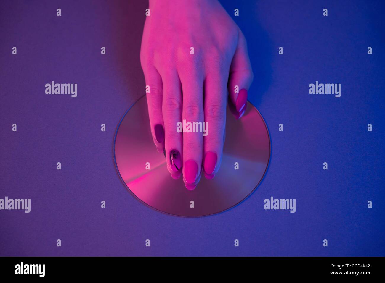 Female hand lies on a CD showing a synthwave manicure. Stock Photo