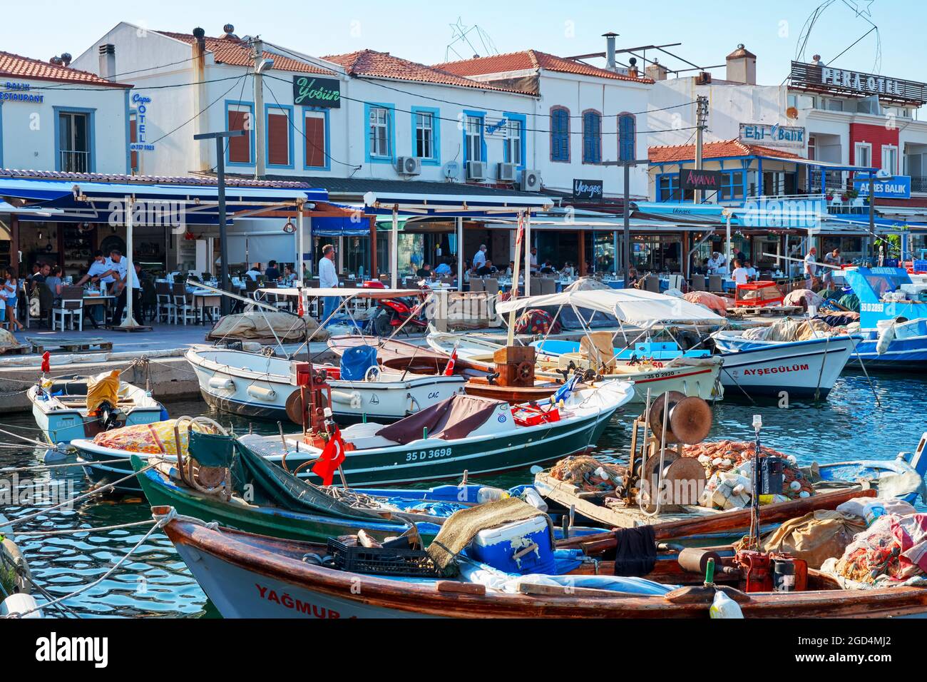 Urla, Izmir, Turkey - June, 2021: Fishing boats, restaurants and dining people at Urla Iskele port or harbor in Turkey. Travel landmarks of Turkey. Stock Photo