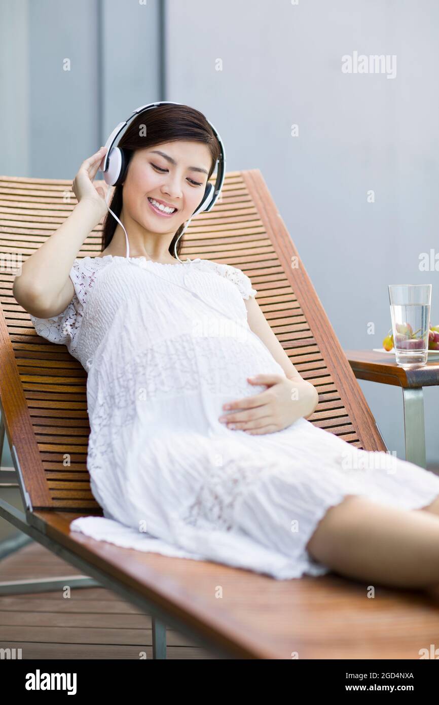 Pregnant woman listening to music on chaise longue Stock Photo - Alamy