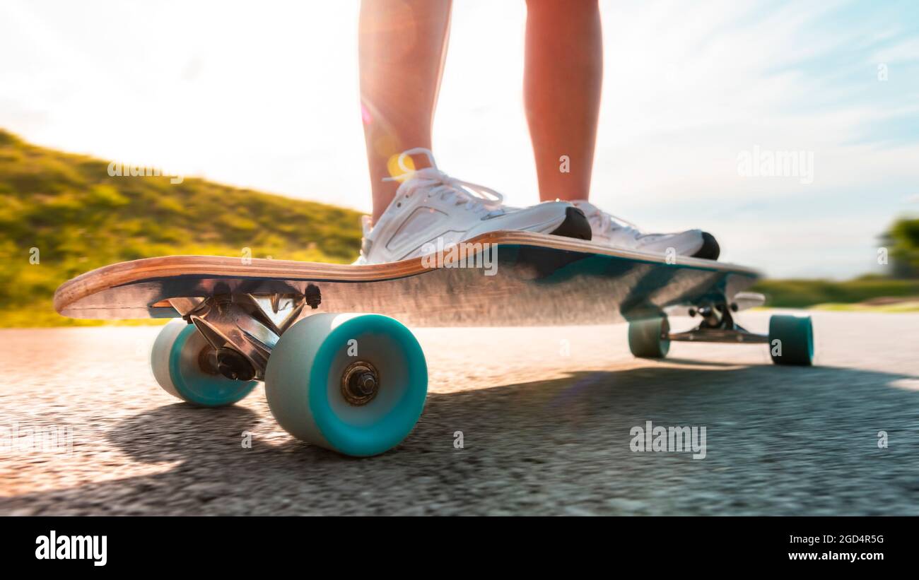 Wide angle longboard in motion at sunny day on the asphalt road. Close up of a spinning wheel. Stock Photo