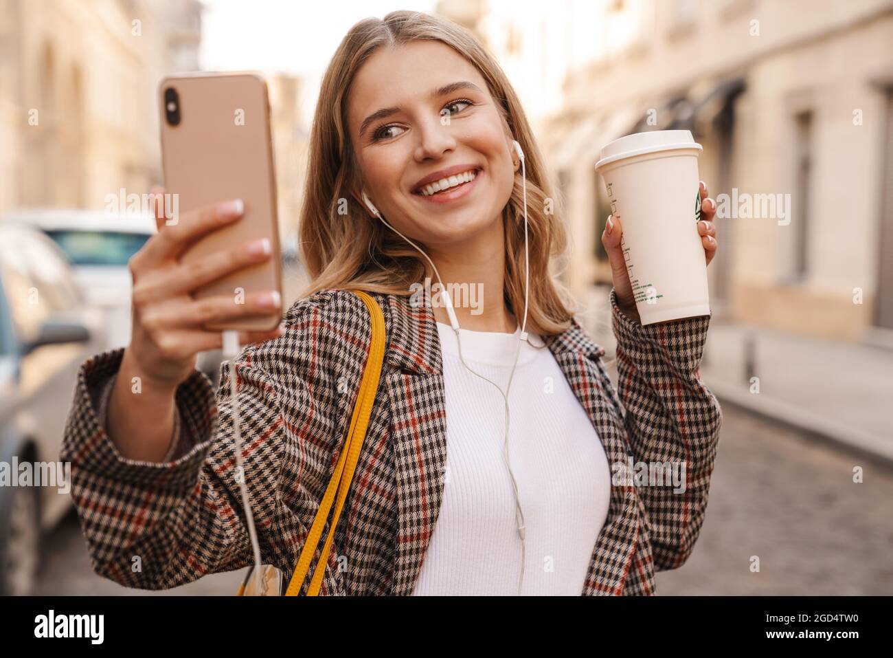 Smiling young blonde woman taking a selfie while walking on a city ...