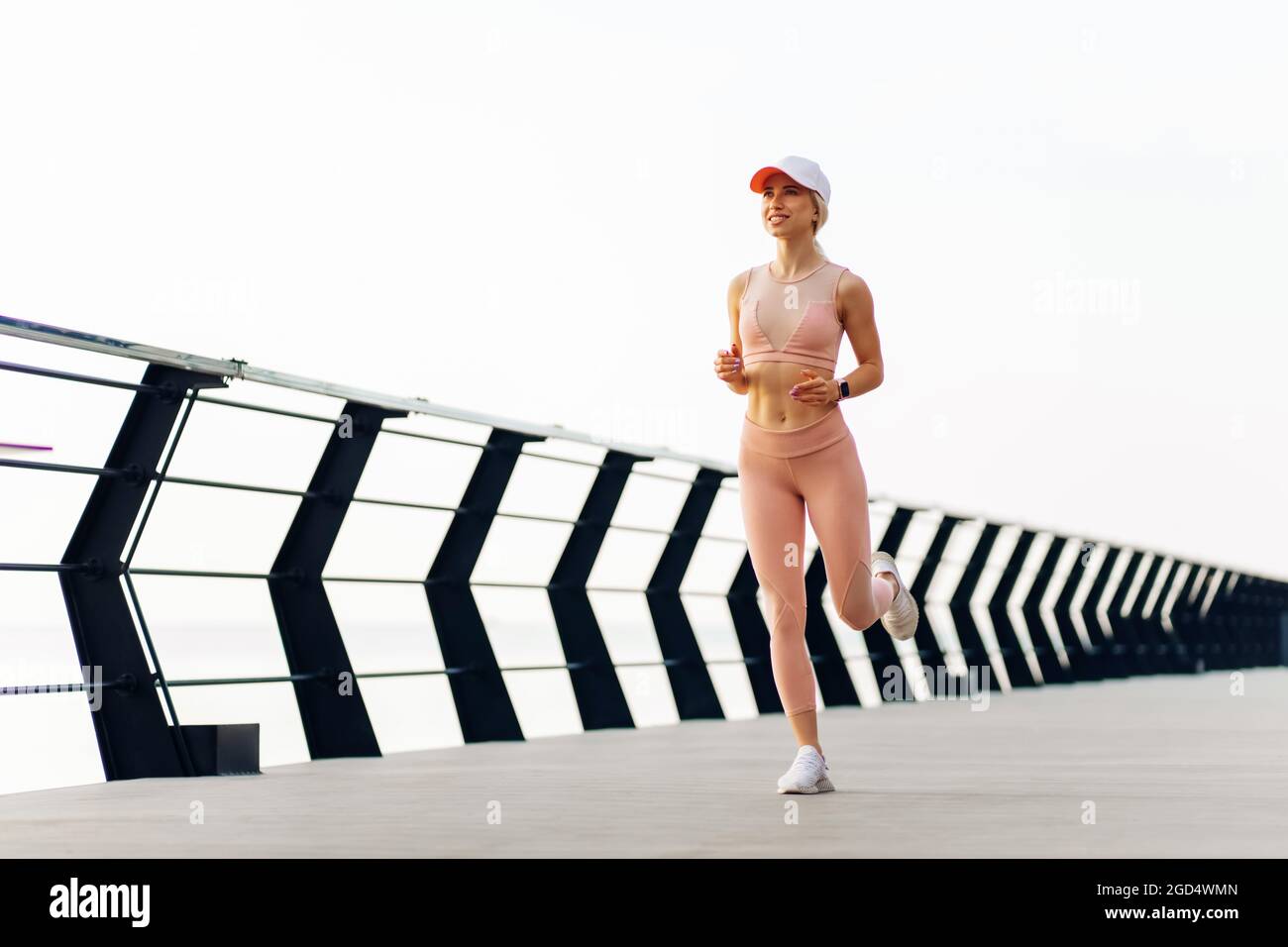 Running young woman, in sports pink clothes, Runner runs in sunny bright light at sunrise, Female fitness model workout outside the city on the embank Stock Photo