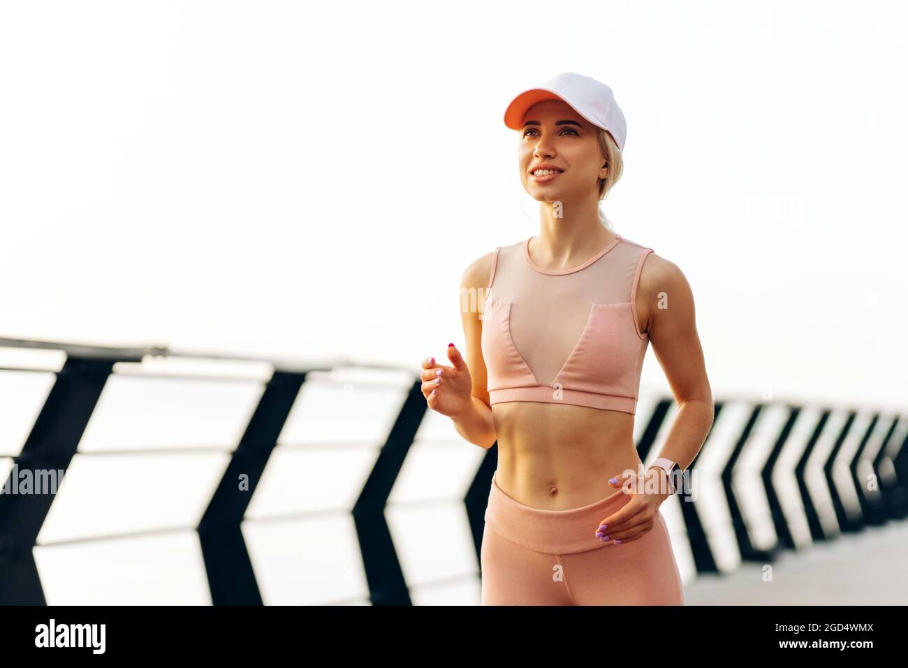 Running young woman, in sports pink clothes, Runner runs in sunny bright light at sunrise, Female fitness model workout outside the city on the embank Stock Photo