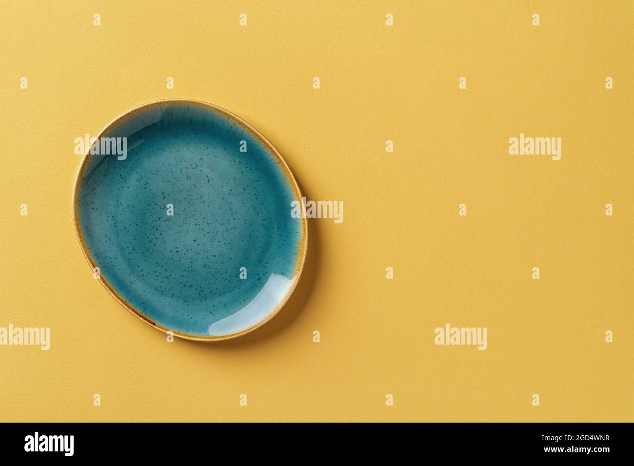 Turquoise teal oval ceramic plate over textured yellow background. Modern trendy colored crockery and tableware for stylish food design. Empty dishes. Stock Photo