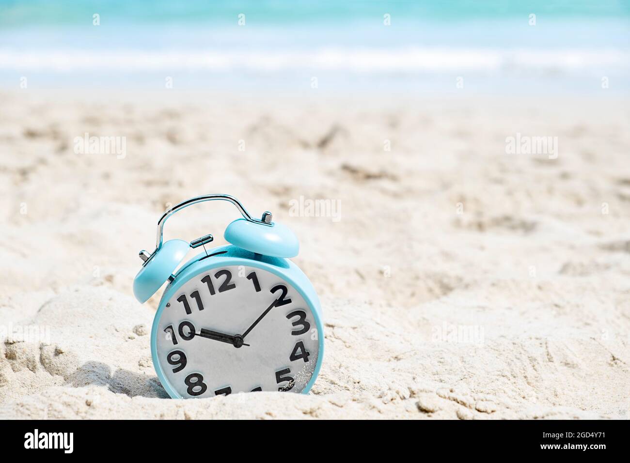 Blue alarm clock on the sand beach by the sea Stock Photo