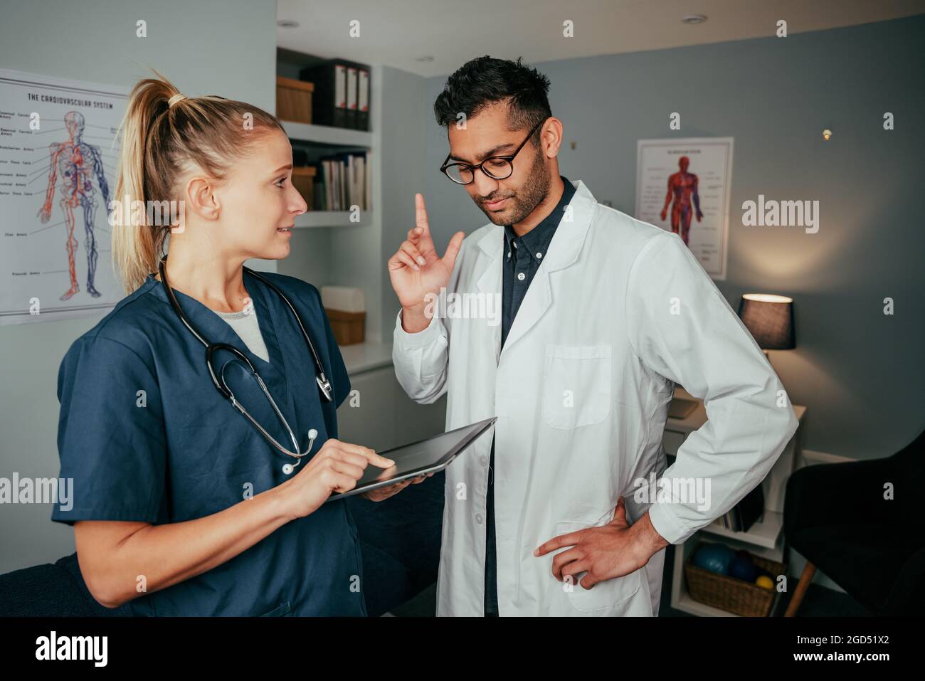 Caucasian female nurse intern chatting to male doctor standing in office holding digital tablet Stock Photo