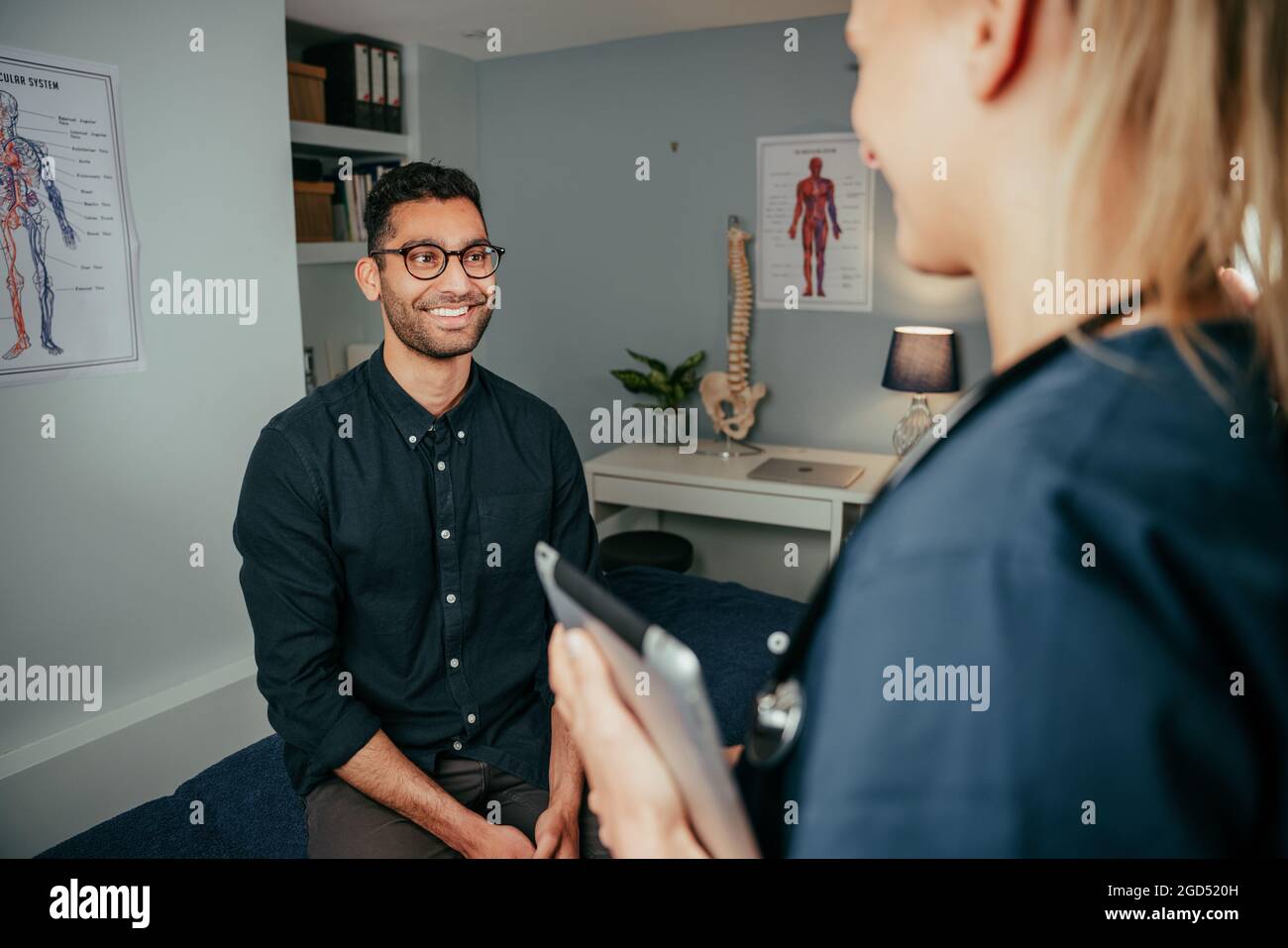 Mixed race male patient chatting to female nurse standing in clinic Stock Photo