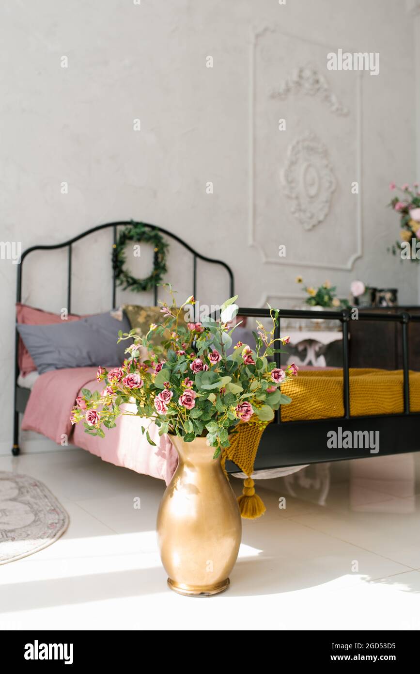 Golden vase with flowers near the bed in the bedroom Stock Photo