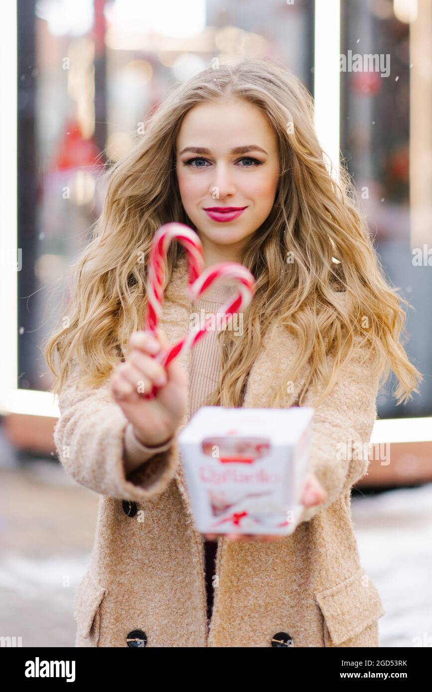 A happy smiling lady poses at a street holiday fair, holding lollipops in her hands. A funny girl makes a heart out of lollipops on a stick. The conce Stock Photo