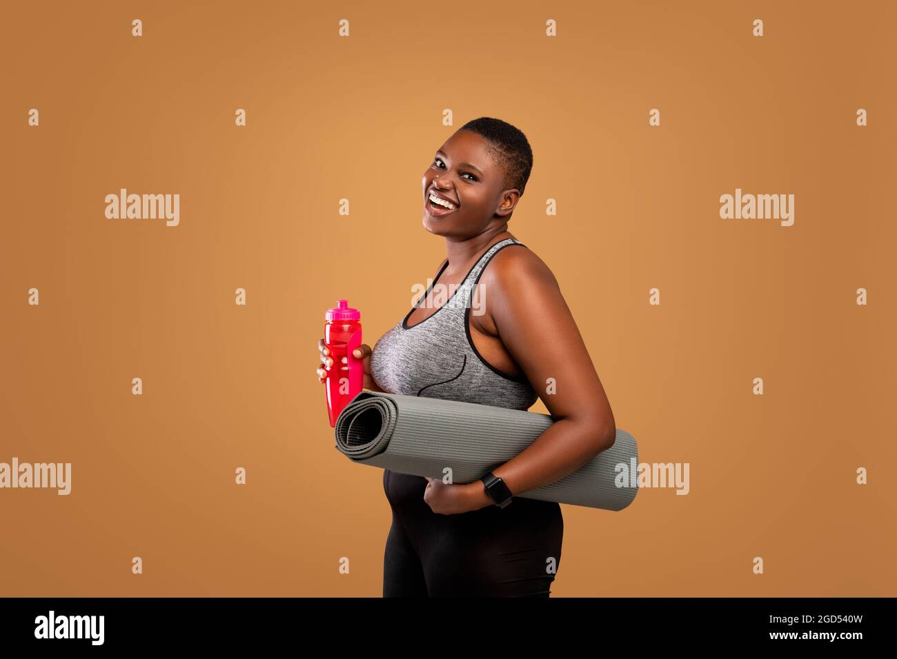 Fitness Concept. Portrait of happy black plus size woman holding water  bottle and yoga mat, body positive female smiling and looking at camera  standin Stock Photo - Alamy