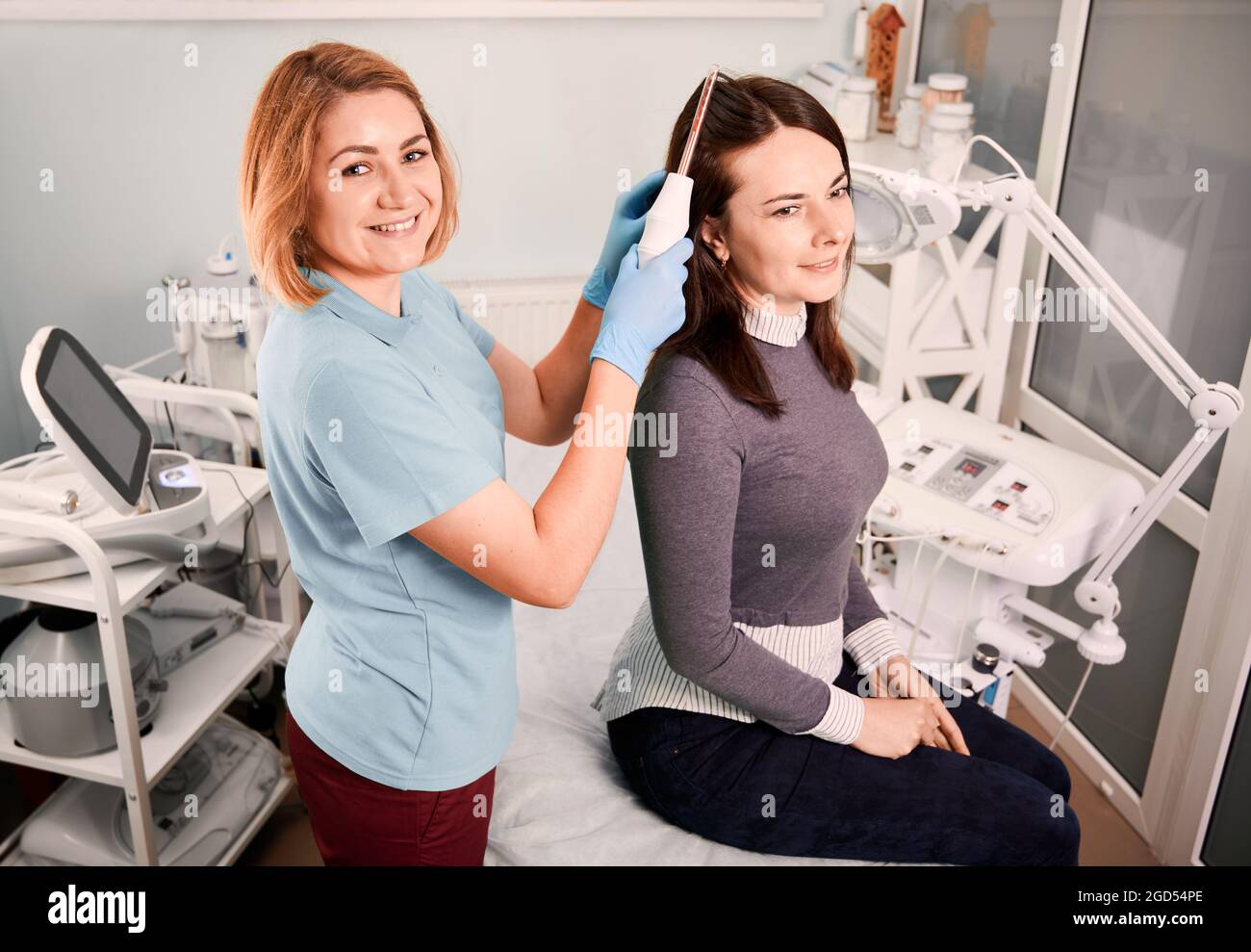 Joyful doctor trichologist brushing female client hair with laser hair