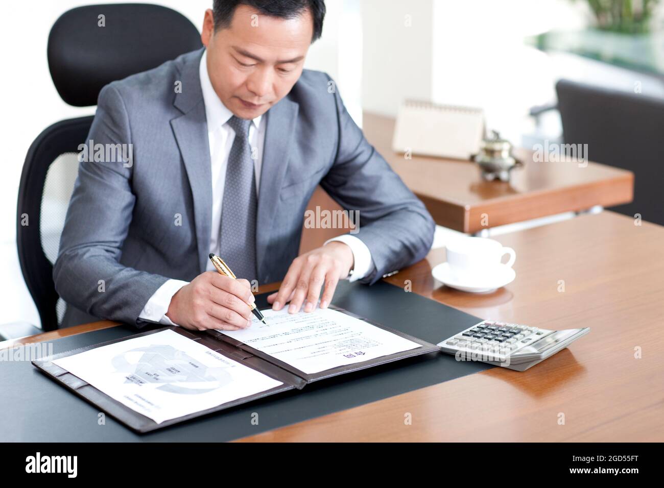 Mature businessman sitting at desk signing a document Stock Photo