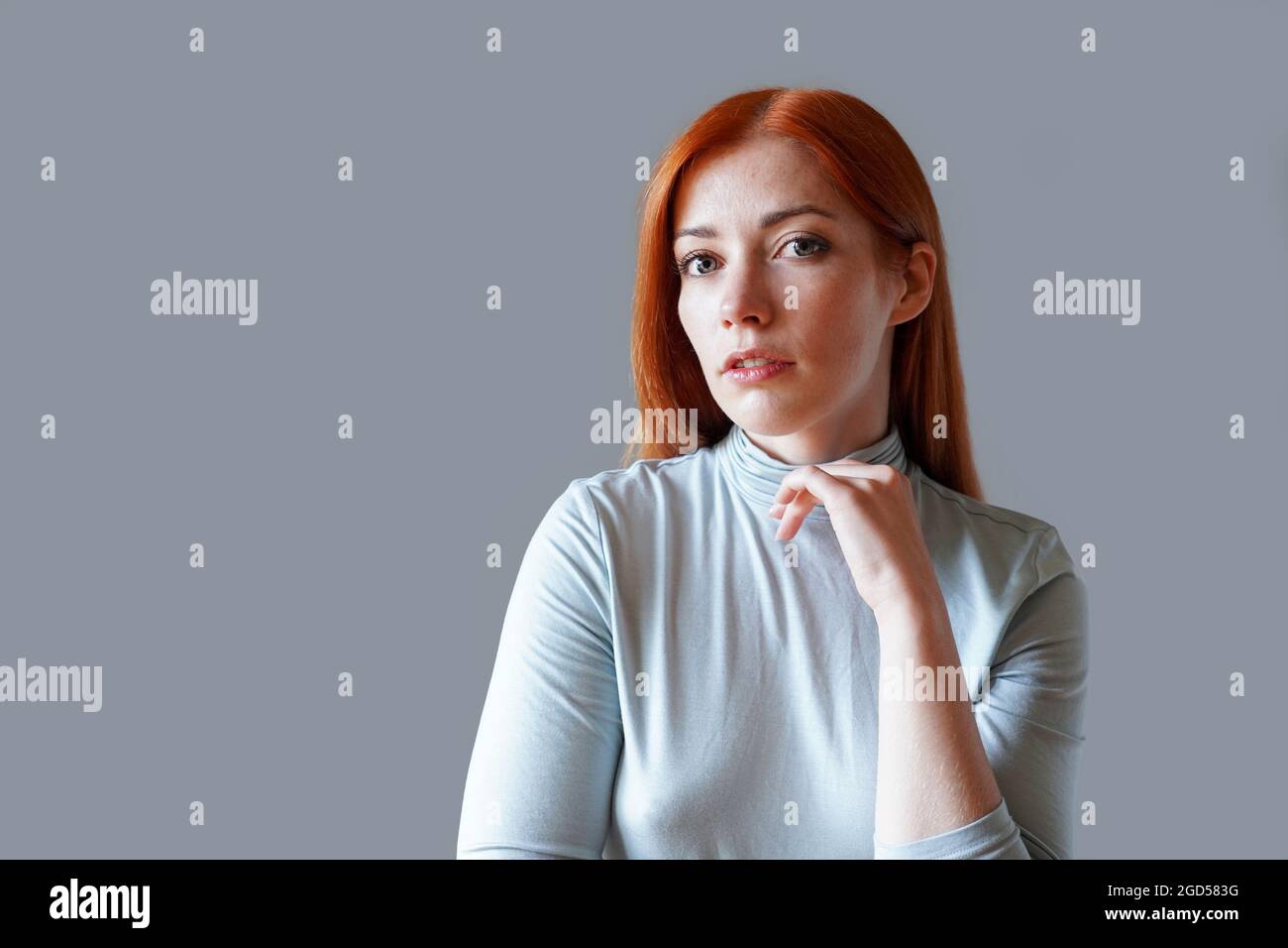 contemplative young woman with long red hair and light blue turtleneck Stock Photo