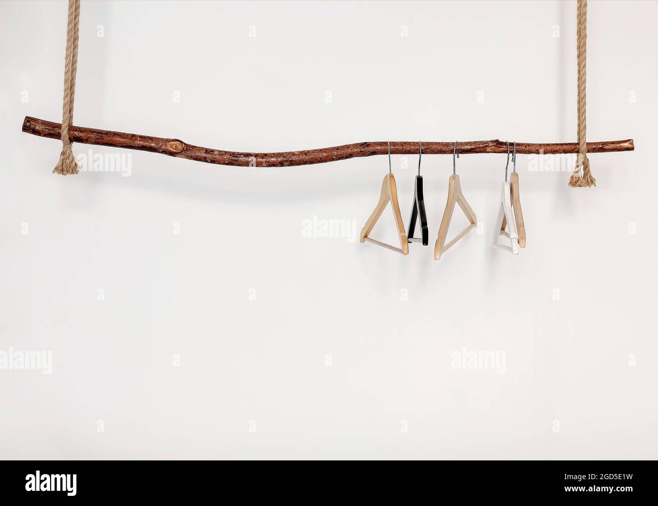 Five empty clothes hangers hanging on wooden rustic style rod on thick rope,  isolated over white wall Stock Photo - Alamy