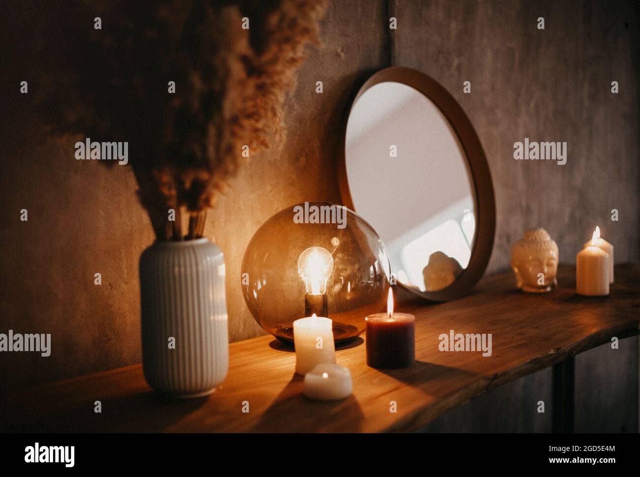 Round mirror on wooden shelf with two burning candles and small