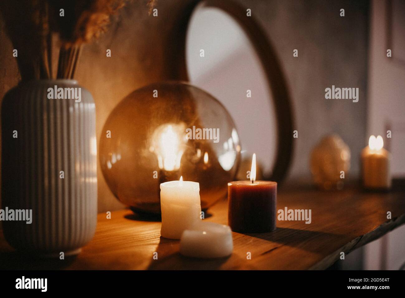 Round mirror on wooden shelf with two burning candles and small