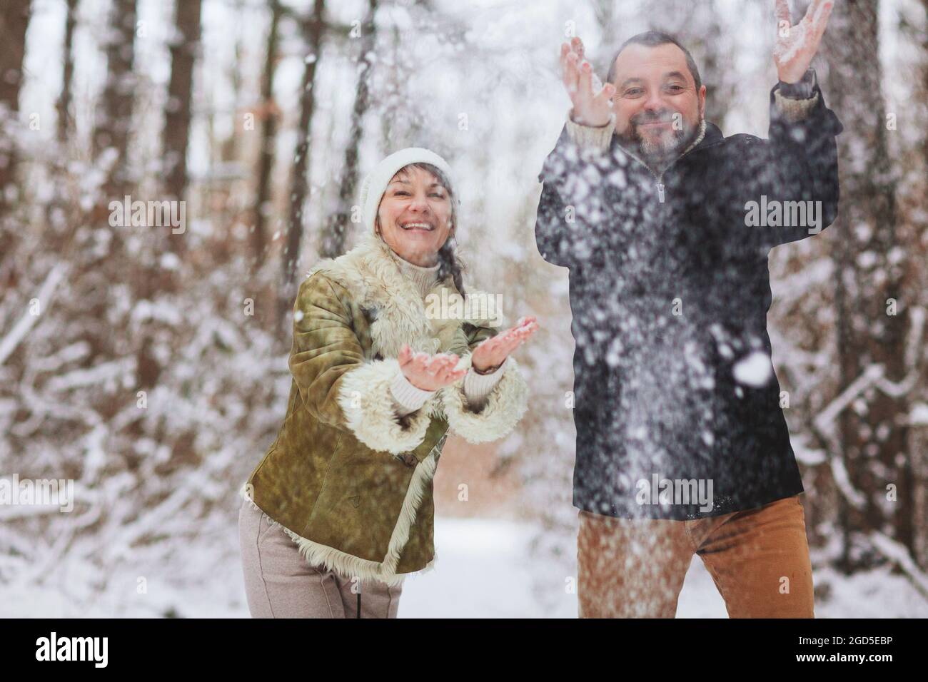Happy playful mature family couple sledding in winter park, laughing and having fun together, positive middle-aged woman and her husband pushing her f Stock Photo