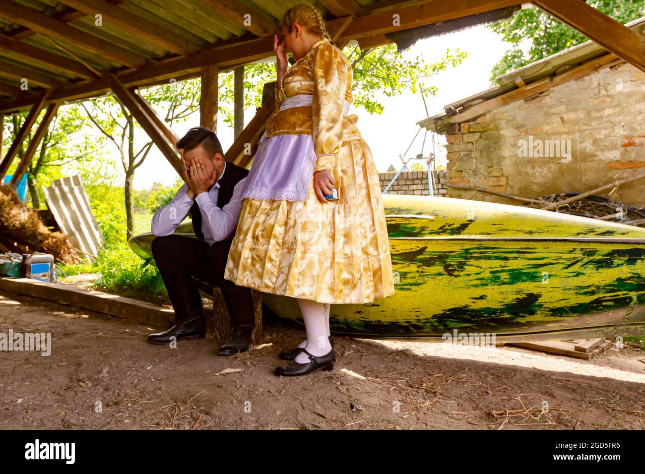 Ivanovo, Vojvodina, Serbia - April 17, 2016: Girl make jokes with young man who is sitting on wooden stump wearing a traditional folk costume in ancie Stock Photo