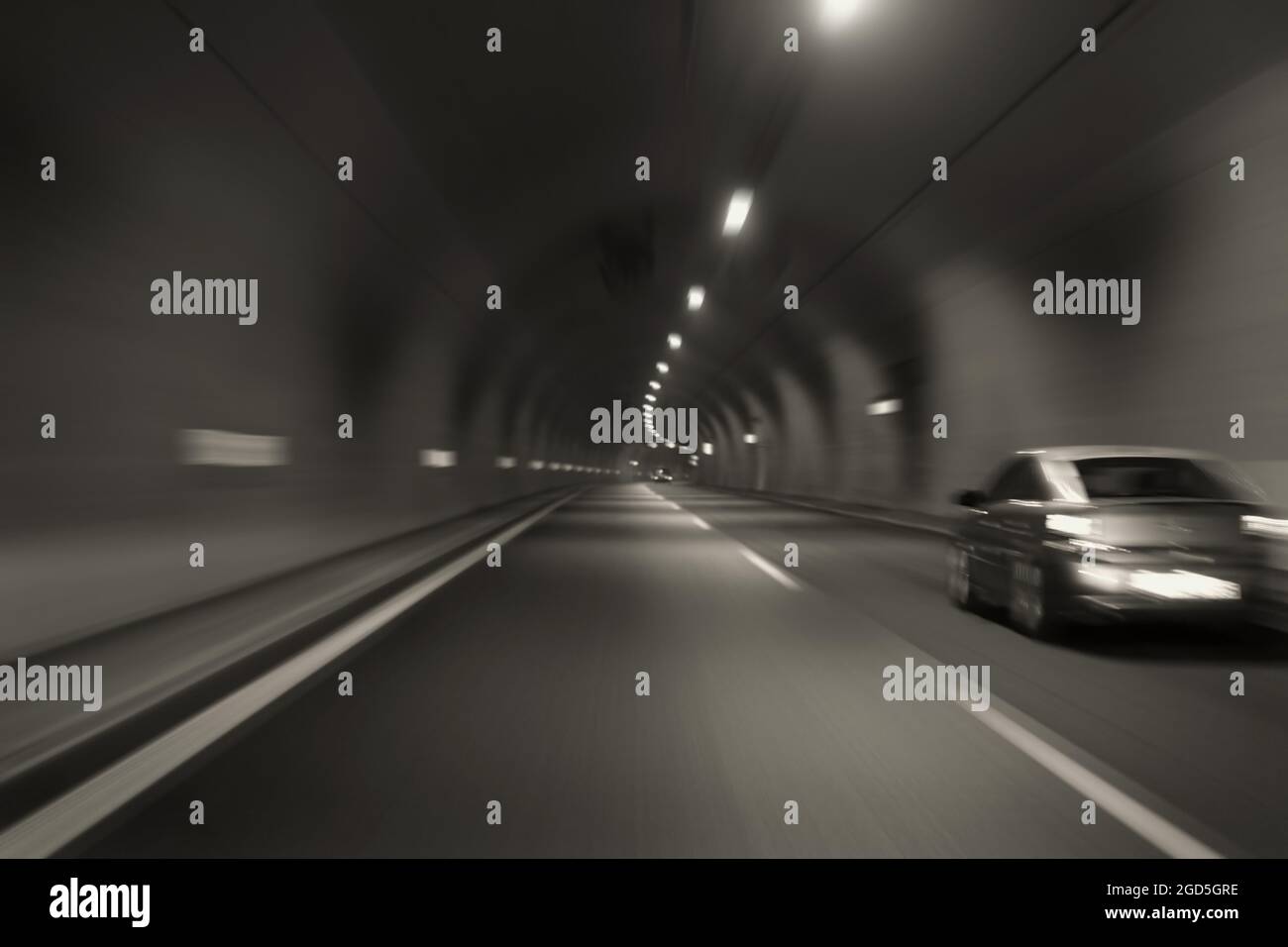 Car speeding through motorway tunnel motion blur. Black and white tint long exposure. Stock Photo