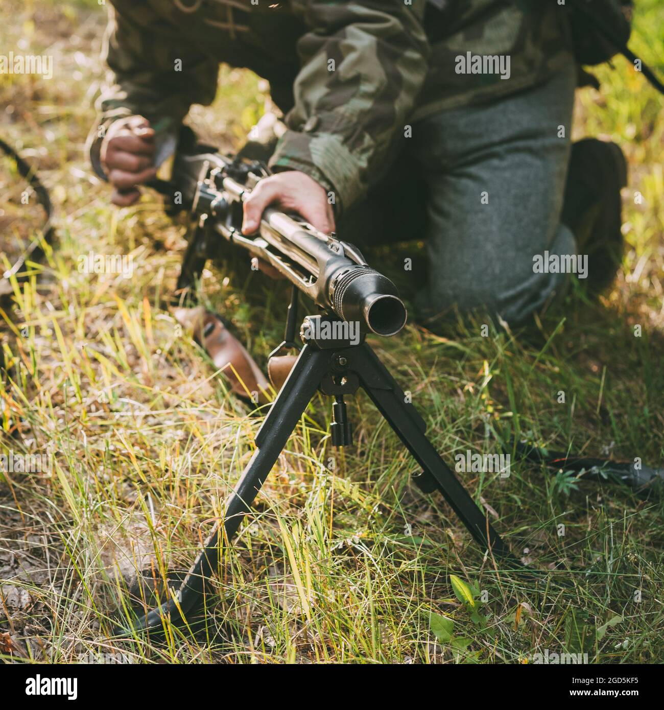 Unidentified re-enactor dressed as German soldier machine-gunner aiming a machine gun at a enemy in forest Stock Photo