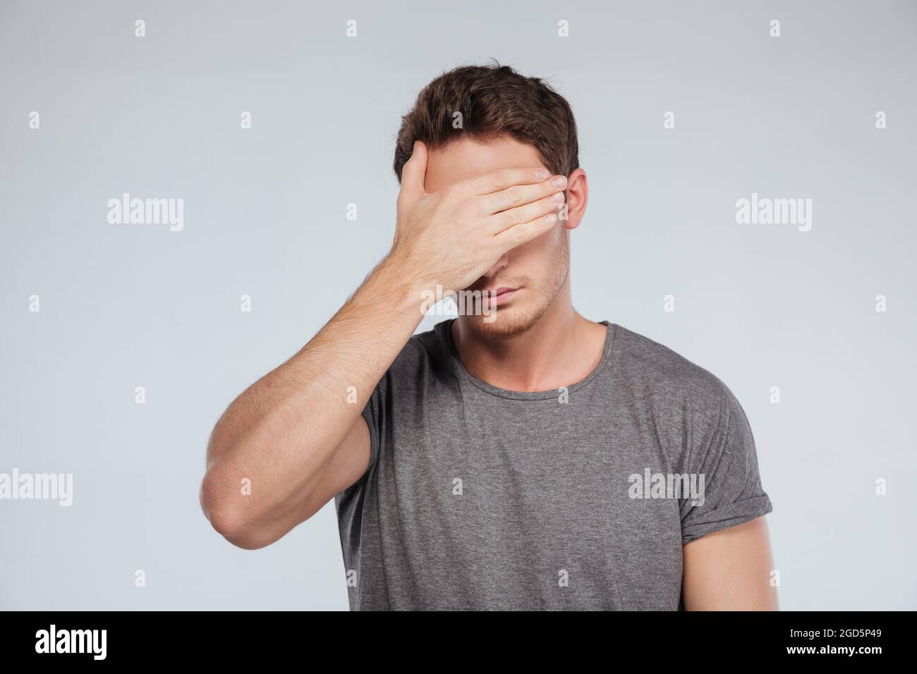Portrait of a young casual man covering eyes with hand isolated on the ...