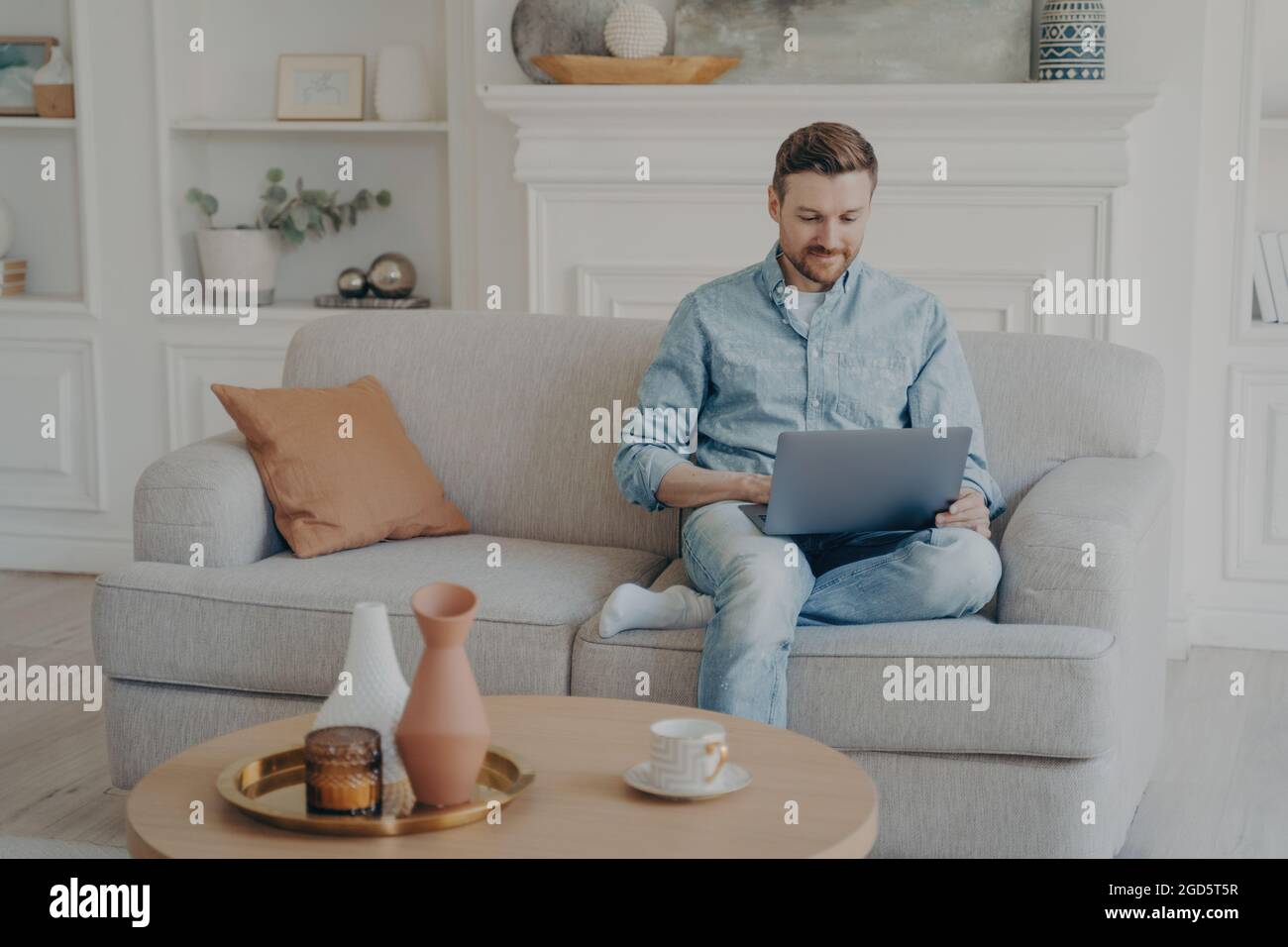 Young office worker working from home while sitting on couch with crossed leg Stock Photo