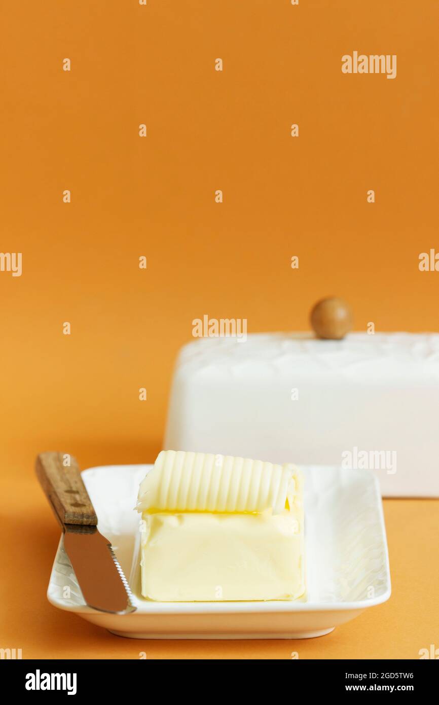 A piece of butter in butter dish and a knife on a colored background. Stock Photo