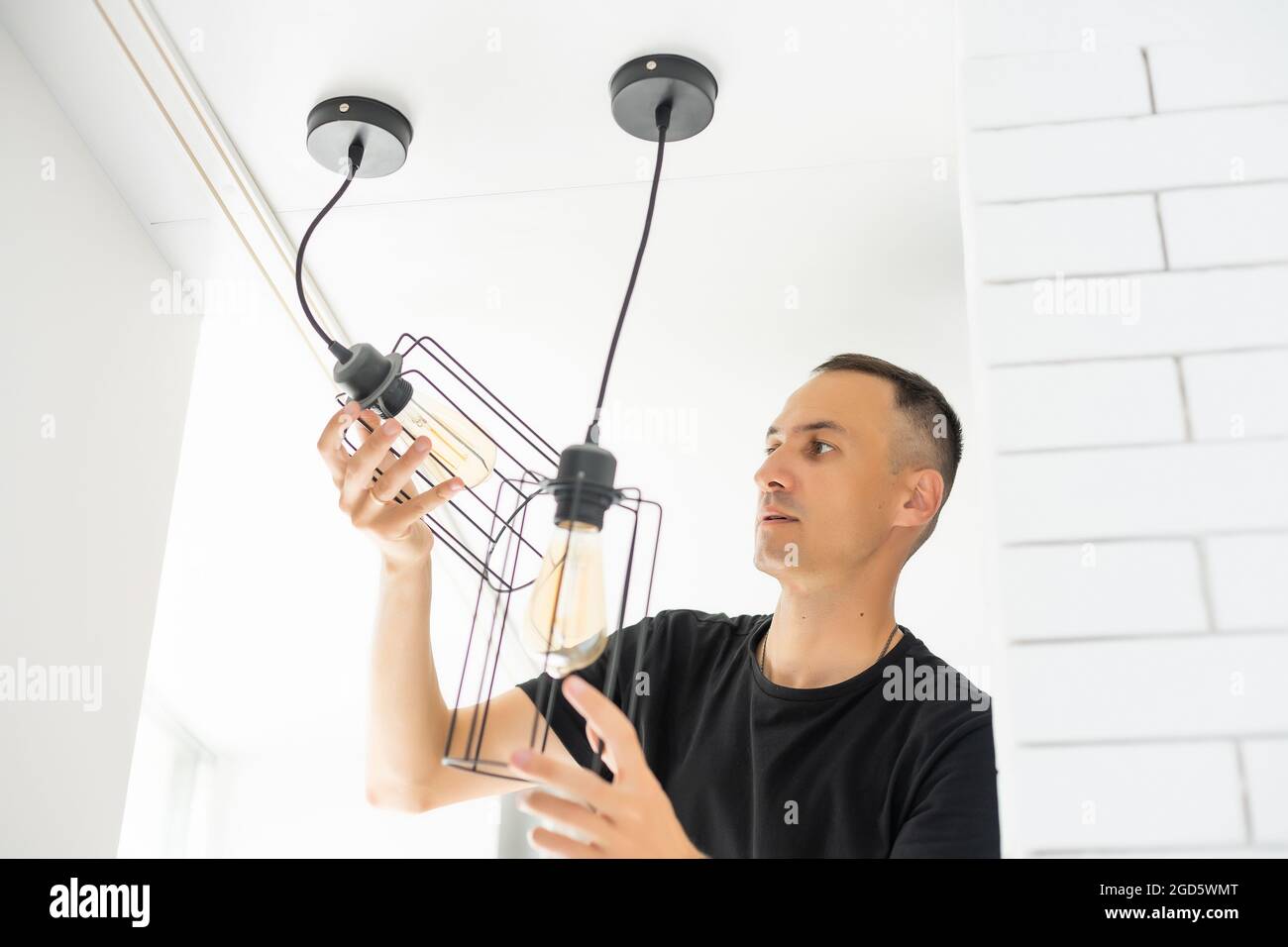 Worker repairing lamp on stretch ceiling indoors Stock Photo