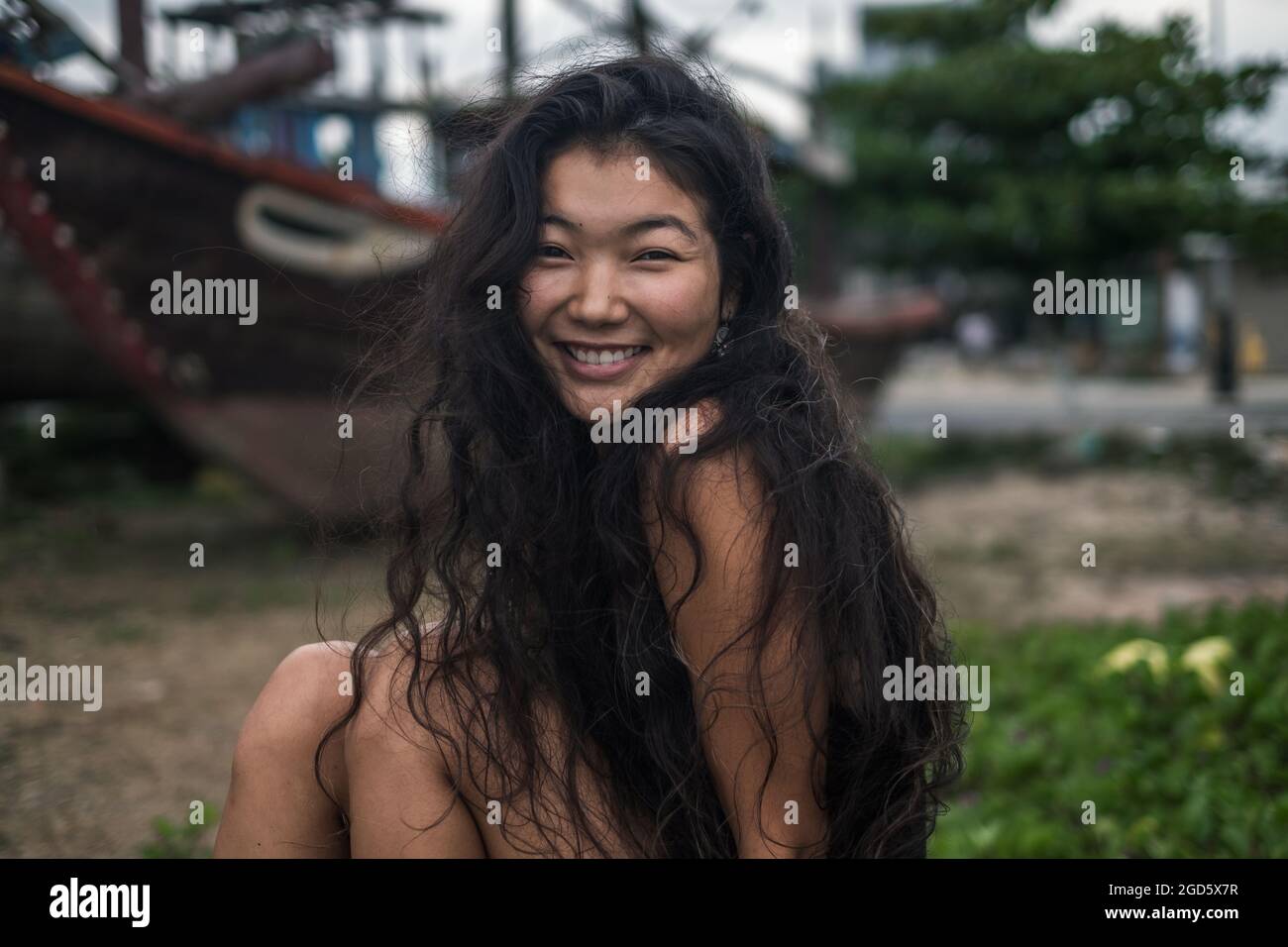 Portrait of smiling charming asian girl. Brunette with long curly hair posing. Looking at camera with copy space. Wind in her hair. . High quality  Stock Photo