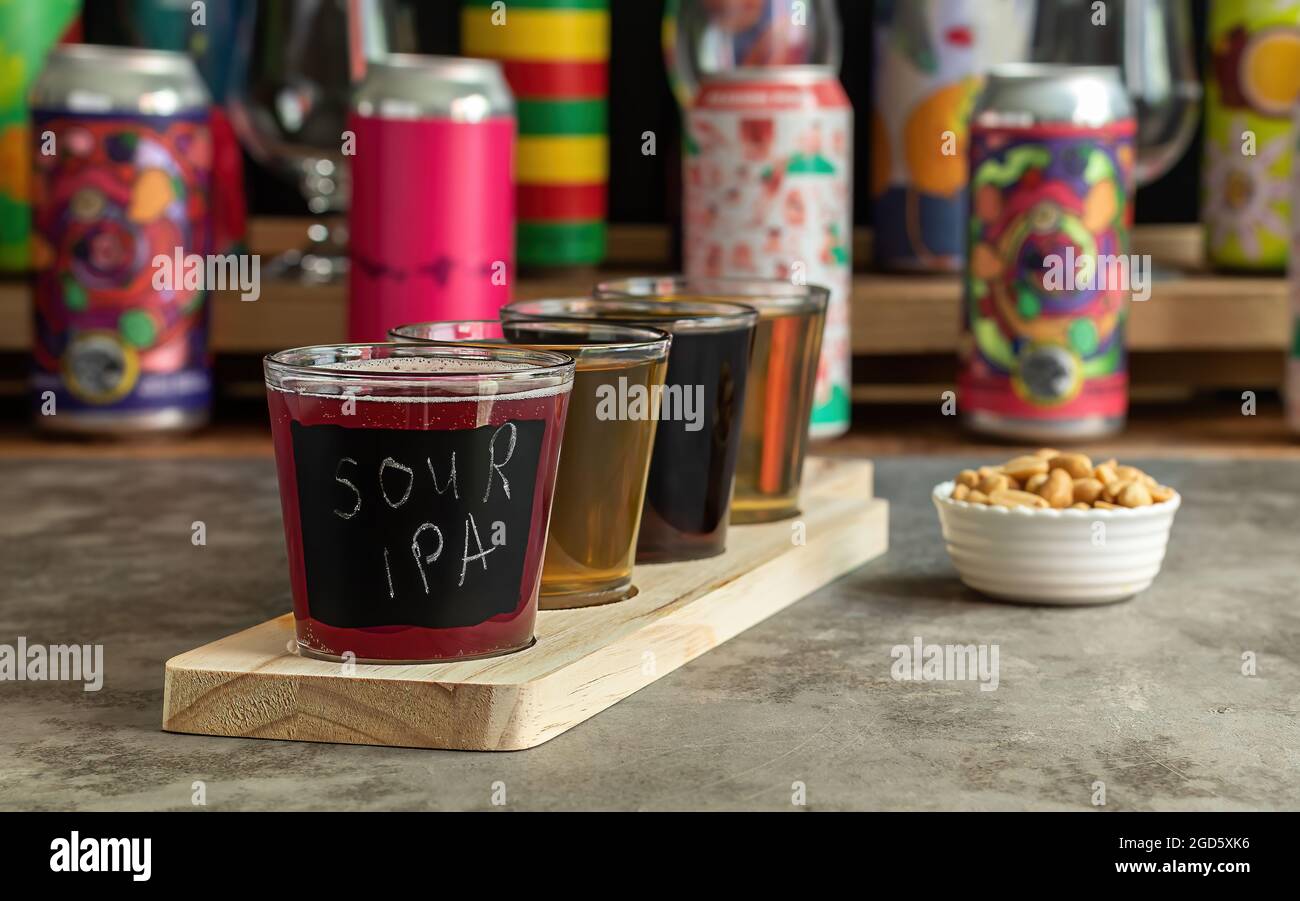 Craft beer tasting, sour fruit IPA, lager, stout, and pale ale. Bar with different cans in the blurred background.  Stock Photo
