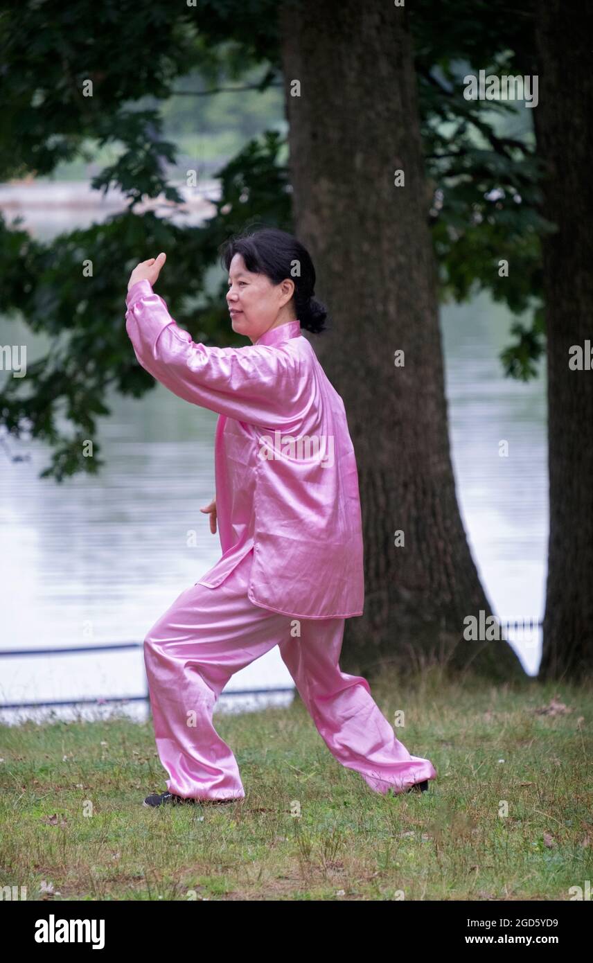 An attractive woman in a shiny pink Tai Chi suit goes through graceful motions in a park in Queens, New York City Stock Photo