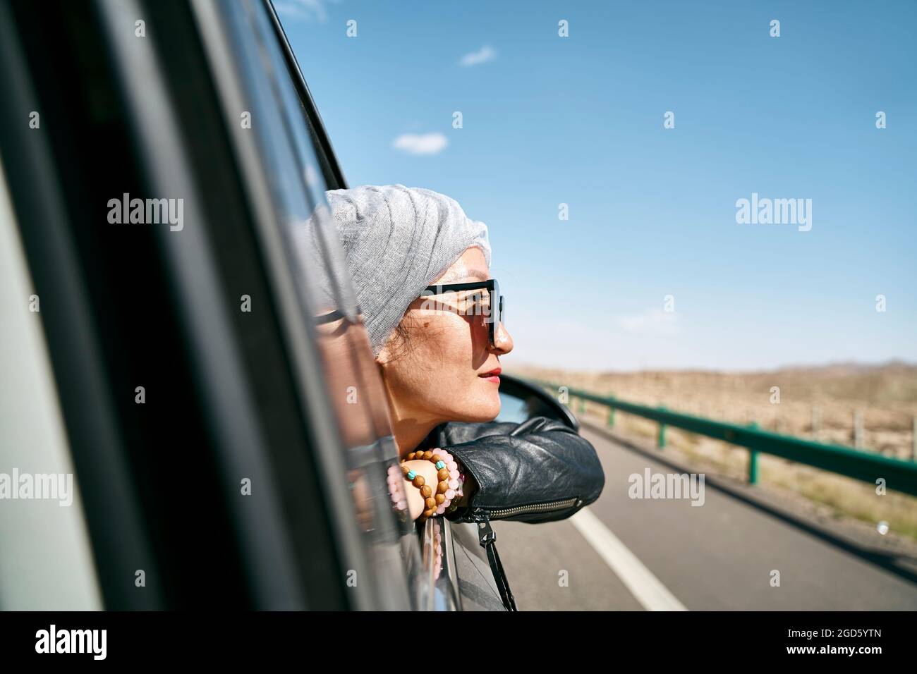 asian woman tourist sticking head out of rear window of a car and enjoying a road trip Stock Photo