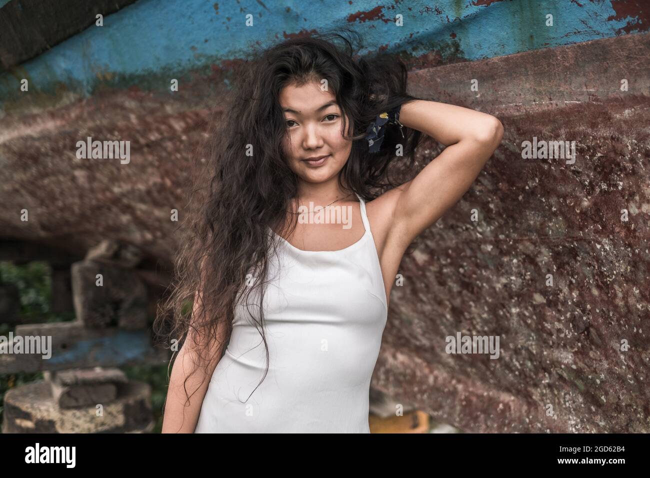 Portrait of beautiful young asian woman wearing white dress and holding hair with hand. Black curly long hair. Looking at camera with copy space Stock Photo