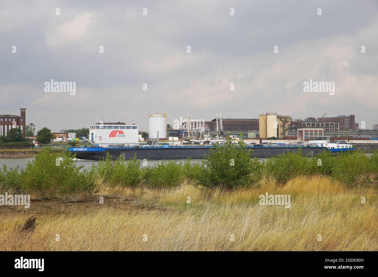 Krefeld (Uerdingen), Germany - July 9. 2021: View over  dry grass on river rhine with inland waterway vessel, industrial area background Stock Photo