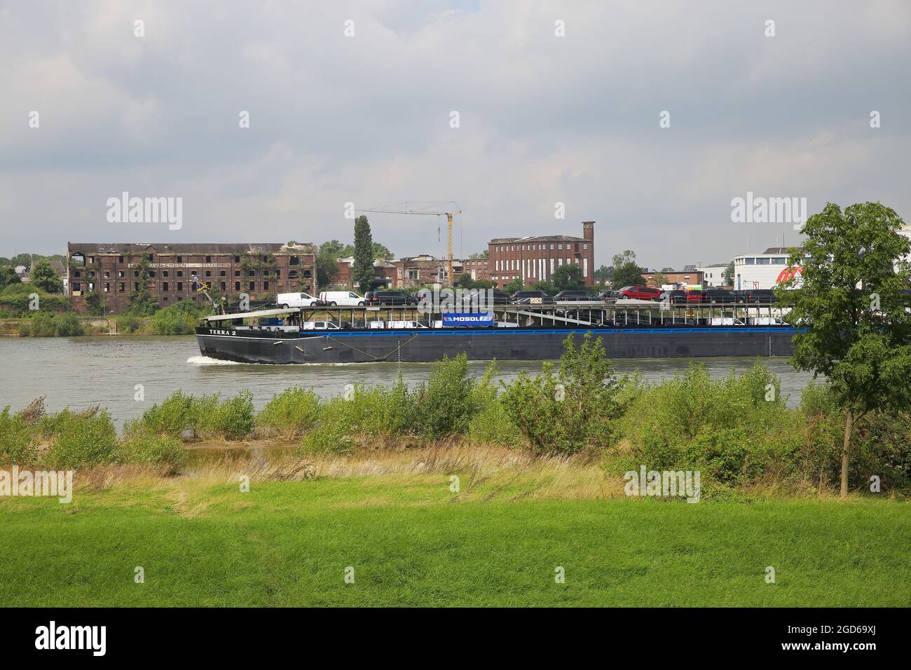 Krefeld (Uerdingen), Germany - July 9. 2021: View over green meadow on river rhine with inland waterway vessel vor vihicle transportation. industrial Stock Photo
