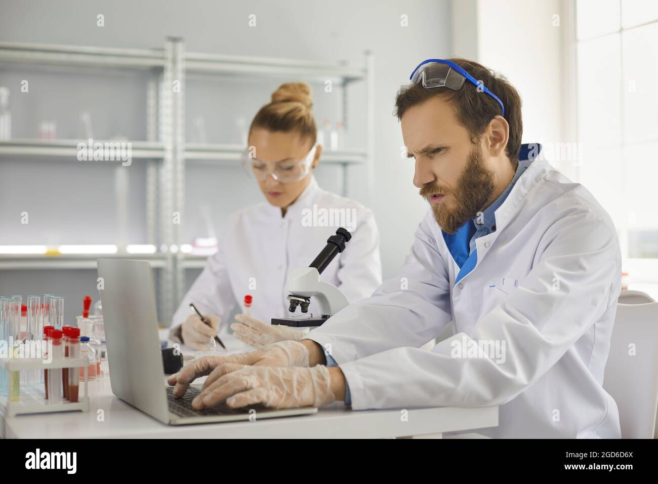 Concentrated scientist typing laptop keyboard working on research report in lab Stock Photo