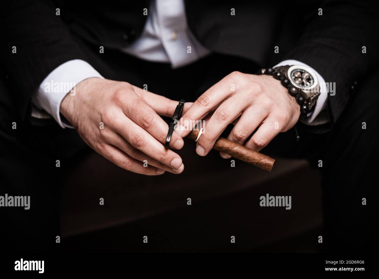 elegant man wearing black suit and white shirt cut Cuban cigar Stock Photo