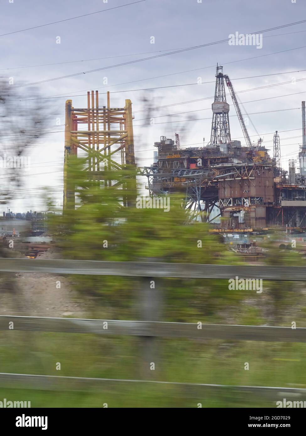 An offshore platform being decommissioned - shot from a moving car, the motion renders the trees fragile and ephemeral, in contrast with the rig. Stock Photo