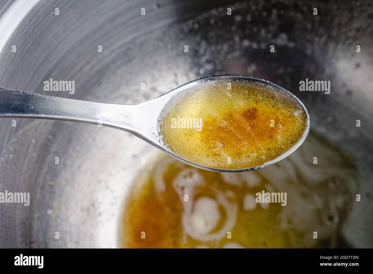 Closeup View of a Tablespoon Full of Browned Butter: Browned butter in a spoon held over a mixing bowl Stock Photo