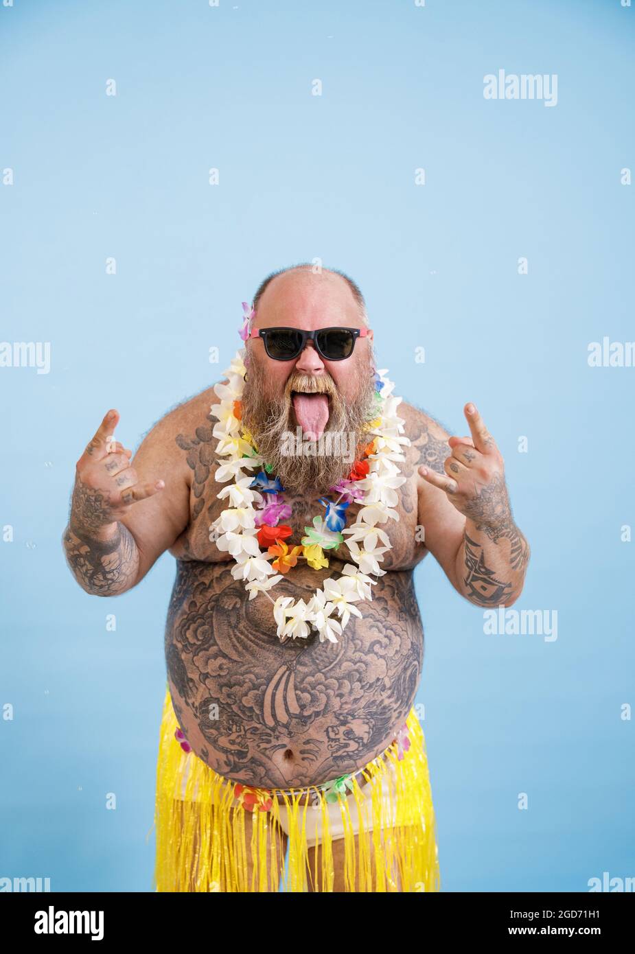 Funny man with overweight and flowers garland shows Horns gestures on light blue background Stock Photo