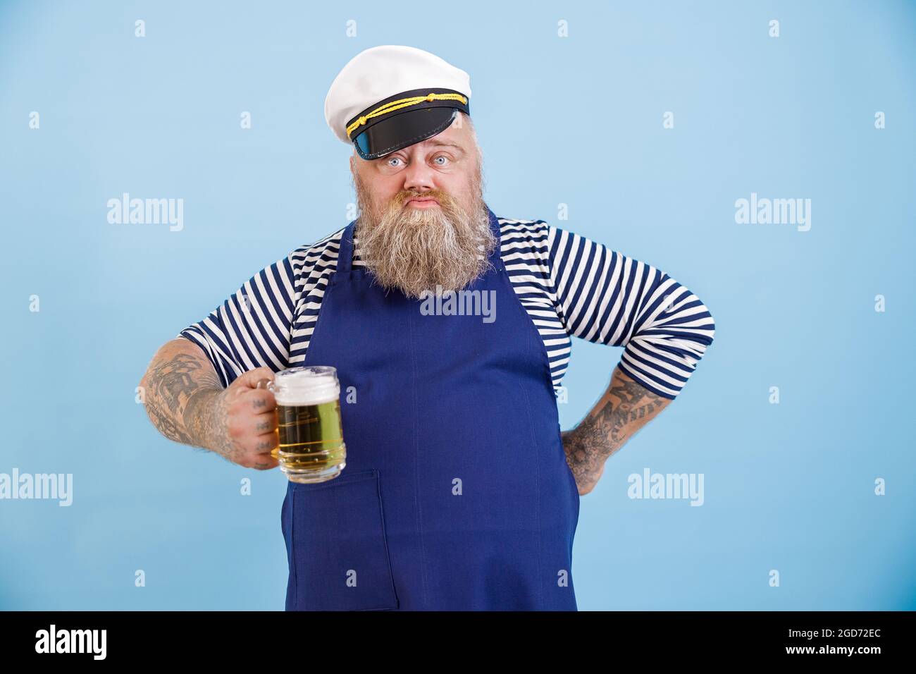 Funny plus size man in sailor suit holds glass of foamy beer on light blue background Stock Photo