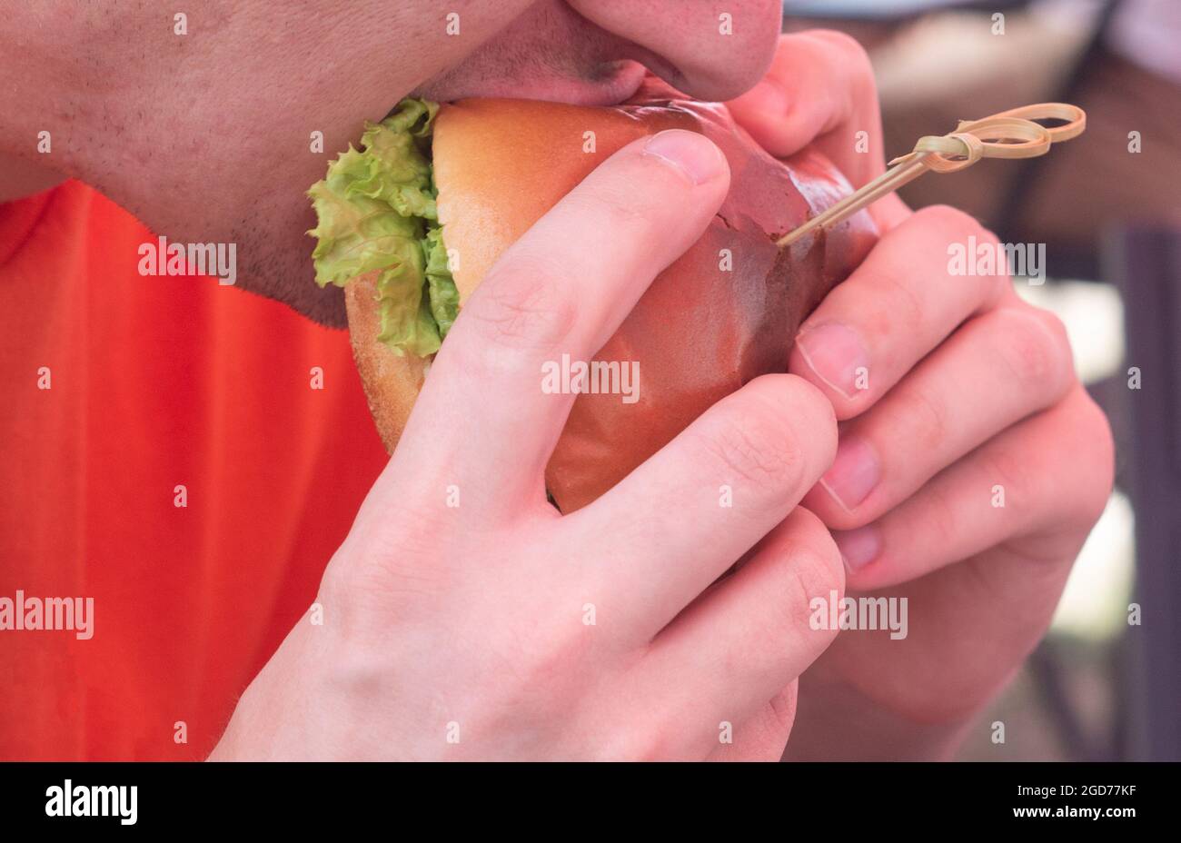 A man eats a big juicy burger in a burger shop. Burger with cheese, vegetables, cutlets close-up. Stock Photo