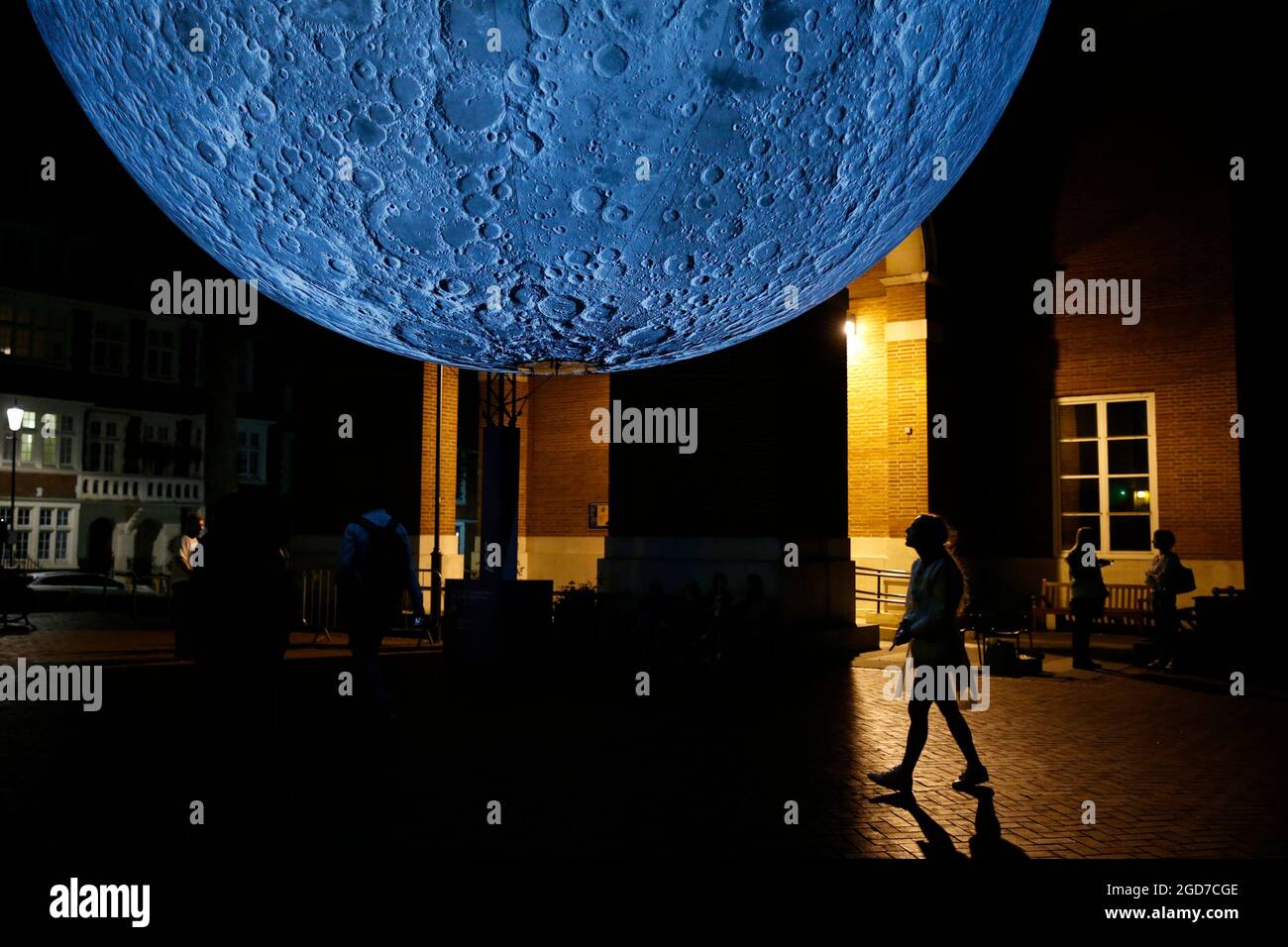 A man walks beneath Luke Jerram's 'Museum of the Moon', a light and sound installation that includes a replica of the moon seven metres in diameter, hangs in Kensington Town Square in London as part of the Kensington + Chelsea Festival. Picture date: Wednesday August 11, 2021. Stock Photo