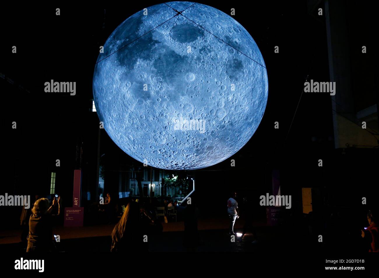 People take photos of Luke Jerram's 'Museum of the Moon', a light and sound installation that includes a replica of the moon seven metres in diameter, hangs in Kensington Town Square in London as part of the Kensington + Chelsea Festival. Picture date: Wednesday August 11, 2021. Stock Photo