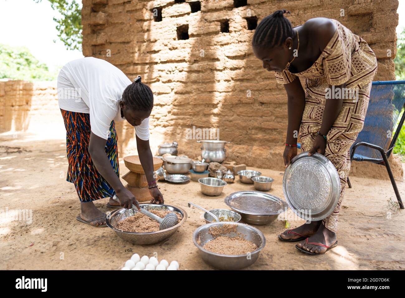 In this image, two young black women are preparing a meal for their family members in outdoor air kitchen in a west african village Stock Photo